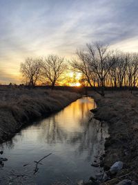 Silhouette bare trees by lake against sky during sunset
