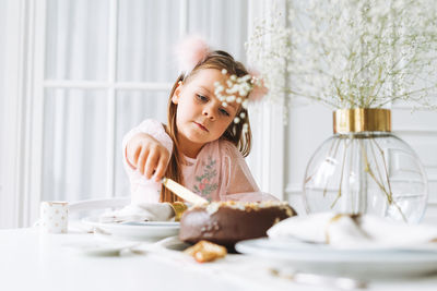 Funny girl in pink dress with chocolate cake on festive table in living room at home, birthday girl