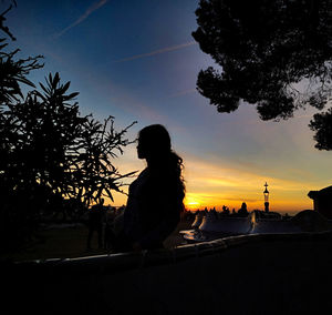 Silhouette woman sitting on beach against sky during sunset