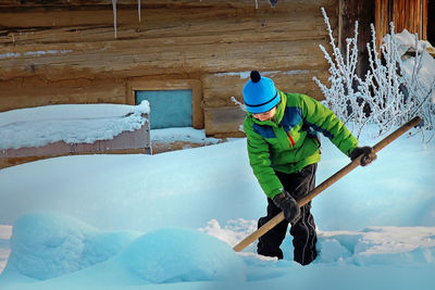 Boy cleaning snow outside cottage