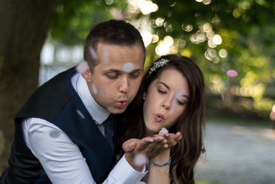 Bride and groom blowing flower petal on palms at park