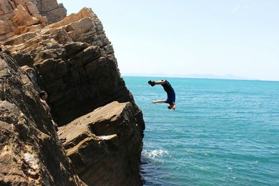 Man diving in sea by rock formation against clear sky on sunny day