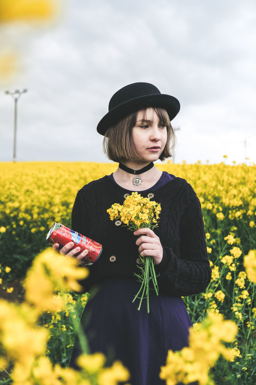 yellow, plant, flower, flowering plant, one person, real people, lifestyles, leisure activity, beauty in nature, fragility, standing, nature, land, field, vulnerability, growth, hat, three quarter length, front view, flower head, outdoors, sunflower