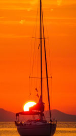Sailboats moored in sea against orange sky