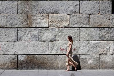 Side view of woman standing against brick wall