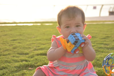 Close-up portrait of baby girl playing with toy car while sitting on grassy field