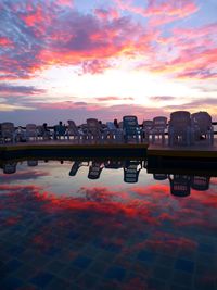 Scenic view of swimming pool by buildings against sky during sunset