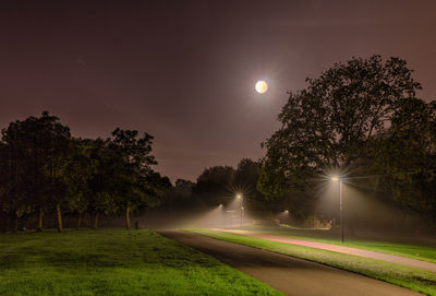 Illuminated street light on field against sky at night