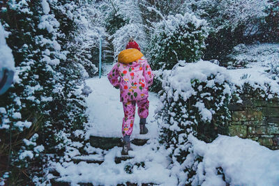 Rear view of girl in a snowsuit climbing up a snowy staircase into a garden