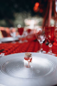 A small red flower in small jar stands on a silver plate against the background of a red tablecloth