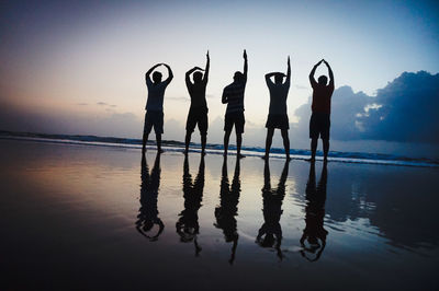 Silhouette of men standing on beach at sunset