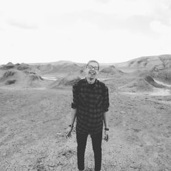 Cheerful young man standing by mud volcanoes against sky