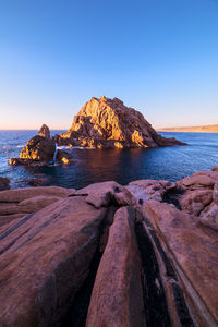 Rock formations on shore against clear sky