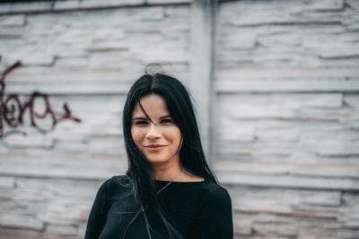 Portrait of smiling young woman standing against wall