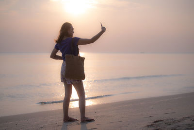 Woman standing on beach against sky during sunset