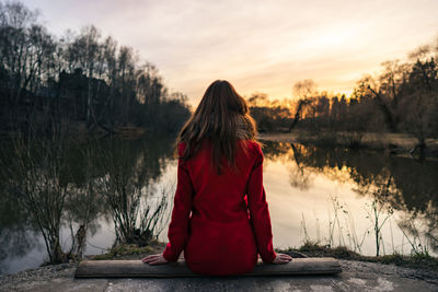 Rear view of woman by lake against sky during sunset