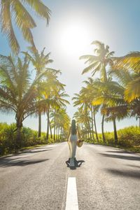 Rear view of woman walking on road amidst palm trees