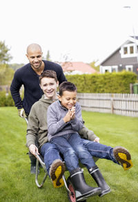 Father pushing children in wheel barrow at yard