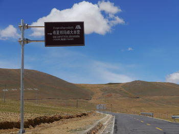 Road sign by country road against blue sky