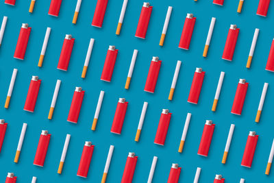 Full frame shot of cigarettes and lighters arranged on blue background