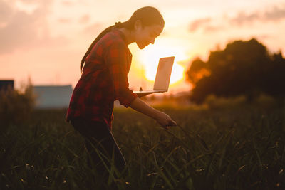 Side view of man standing on field against sky during sunset