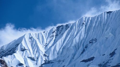 Low angle view of snow covered mountain against blue sky