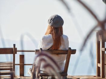 Rear view of woman sitting on chair against sky