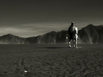 Man riding horse in desert against mountains