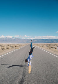 Woman doing handstand on road against clear blue sky