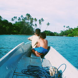 Siblings sitting in boat on lake against sky