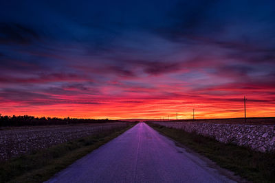 Empty road amidst field against sky during sunset