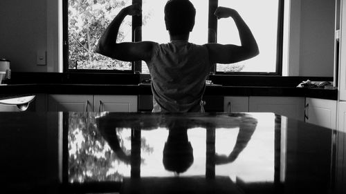 Rear view of man flexing muscles in kitchen at home