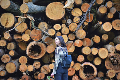 Rear view of woman with backpack standing by woodpile in forest