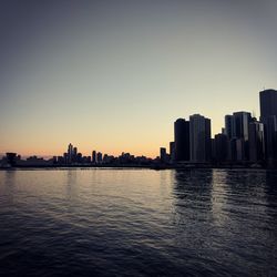 Silhouette buildings in city against clear sky during sunset