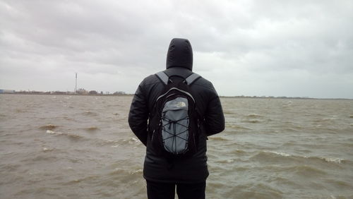 Rear view of man standing at beach against sky