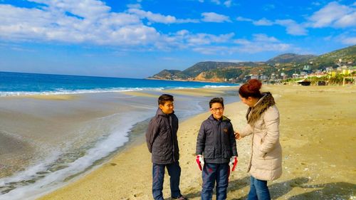 Moth talking with sons while standing at beach against sky