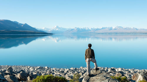 Rear view of man standing by lake against sky