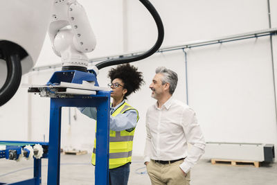 Engineer analyzing robotic arm machine standing by businessman in factory