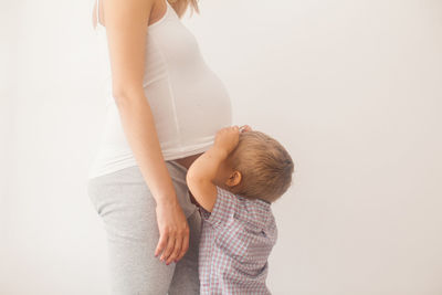 Midsection of mother and son standing against white background