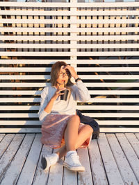 Woman with cup of coffee meets sunset on wooden pier. female with curly hair is enjoying nature