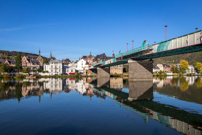 Bridge over river by buildings against clear blue sky