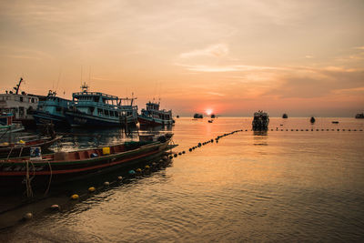 Boats moored at harbor against sky during sunset