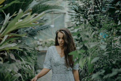 Young woman looking down while standing against plants