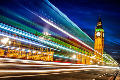 Light trail on westminster bridge with illuminated big ben against sky