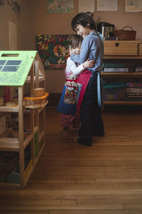 Happy siblings embracing while standing on hardwood floor at home