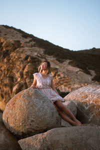 Woman leaning on rock against sky