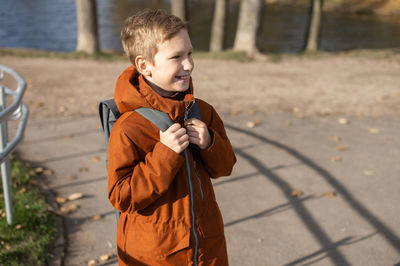 Cute boy holds a backpack and walks down the street in autumn