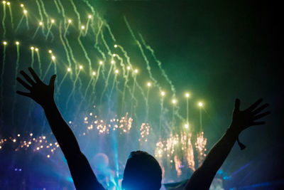 Silhouette man with arms raised enjoying firework display at night