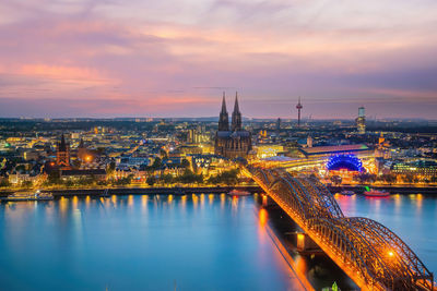 Illuminated bridge over river against sky at sunset