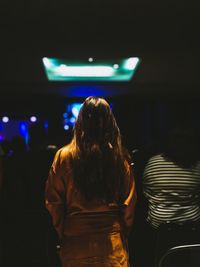 Rear view of woman walking in illuminated bus